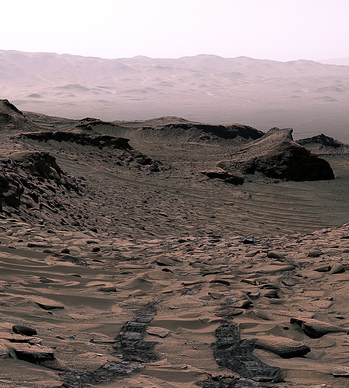 A rover traversing the red rocky surface of Mars with layered terrain and a dusty horizon behind it.